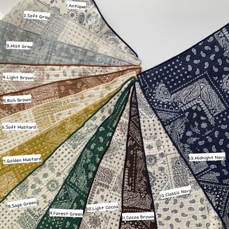 May include: A collection of thirteen square fabric bandanas arranged in a fan shape, each featuring a white paisley pattern. Colors include Antique, Soft Gray, Mist Gray, Light Brown, Rich Brown, Soft Mustard, Golden Mustard, Sage Green, Forest Green, Light Cocoa, Cocoa Brown, Classic Navy, and Midnight Navy.