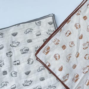 May include: Two white cotton handkerchiefs with repeating patterns of cats and pastries. One handkerchief has a gray border, and the other has a brown border. The cat illustrations are in gray and brown, and the pastries are in brown.