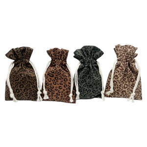 Pode incluir: Quatro pequenas bolsas de cordão com um design de estampa de leopardo. As bolsas são feitas de tecido marrom com manchas pretas e têm cordões brancos.