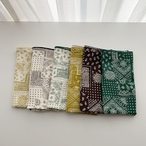 Puede incluir: Un conjunto de seis pa&ntilde;os de tela rectangulares con textura acolchada y un patr&oacute;n de bandana de cachemira repetitivo. Los pa&ntilde;os est&aacute;n dispuestos uno al lado del otro en una fila, mostrando una paleta de colores crema, beige, verde oliva, marr&oacute;n oscuro y verde bosque.