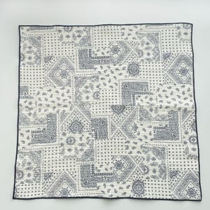 Puede incluir: Un pa&ntilde;uelo cuadrado de tela con un dise&ntilde;o de patchwork de motivos florales y de cachemira en azul oscuro sobre un fondo blanco. El tejido tiene un borde fino de color azul oscuro en los cuatro lados, creando un patr&oacute;n repetitivo de formas geom&eacute;tricas.