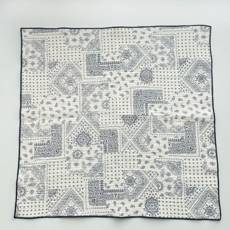 Puede incluir: Un pa&ntilde;uelo cuadrado de tela con un dise&ntilde;o de patchwork de motivos florales y de cachemira en azul oscuro sobre un fondo blanco. El tejido tiene un borde fino de color azul oscuro en los cuatro lados, creando un patr&oacute;n repetitivo de formas geom&eacute;tricas.