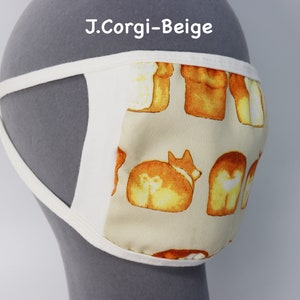 Op de afbeelding: Een beige mondkapje met een herhalend patroon van ge&iuml;llustreerde corgi-honden en broden. Het masker heeft witte stoffen randen en witte zijbanden. De tekst J.Corgi-Beige is in het wit boven het masker op de grijze achtergrond gedrukt.