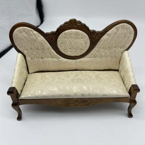 May include: Miniature wooden sofa with a cream-colored floral patterned seat and back. The back has a decorative carved wooden frame and a diamond-stitched center. The sofa has curved arms and legs.