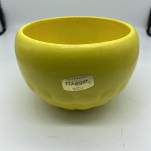 Op de afbeelding: Een ronde, gele keramische kom met een getextureerde buitenkant. De kom heeft een gladde binnenkant en een label met de tekst "Copyrighted Haeger, Macomb, ILL, Made in USA."