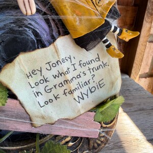Peut inclure: Une figurine portant un imperm&eacute;able jaune et des chaussettes ray&eacute;es noires et blanches, tenant un papier avec le texte : Hey Jonesy, Look what I found in Gramma's trunk. Look familiar? Wybie. La figurine est d&eacute;cor&eacute;e de toiles d'araign&eacute;e artificielles.