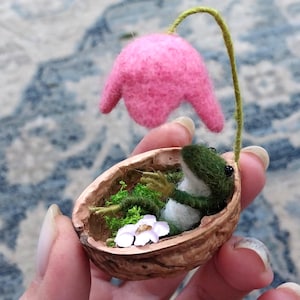Rana bebé en miniatura hecha a mano con fieltro de aguja en una cáscara de nuez con flor