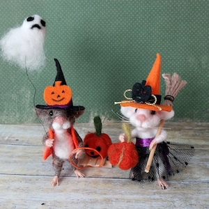 May include: Two felt mice dressed in Halloween costumes. One mouse wears a witch hat with a black and orange pumpkin and holds a broom. The other mouse wears a witch hat with a black and orange pumpkin and holds a string with a white ghost attached to it. Both mice are holding orange pumpkins.