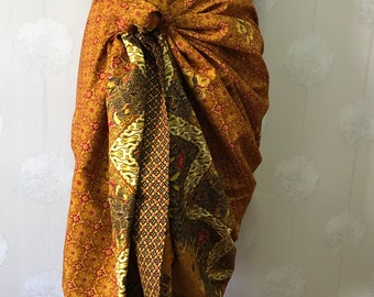 May include: A brown and gold patterned sarong with a red and gold floral design. The sarong is tied around the waist and draped over the hips.