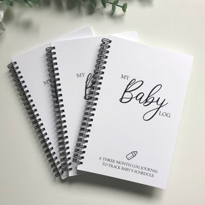May include: Three white spiral-bound journals with black wire binding. The cover features the text "MY Baby LOG" in black, a small baby bottle icon, and the text "A THREE MONTH LOG JOURNAL TO TRACK BABY'S SCHEDULE" printed in black ink.