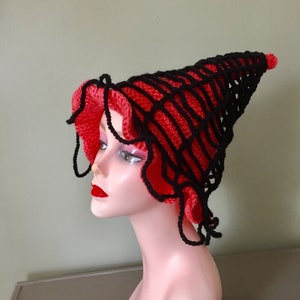 May include: A red and black crocheted witch hat with a pointed crown and a wide brim. The hat is made with a combination of black and red yarn, creating a unique and eye-catching design.