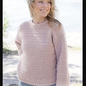 May include: A light pink crochet sweater with a crew neck and long sleeves. The sweater has a textured stitch pattern and is worn by a person. The image includes the text "DROPS DESIGN" and "www.garnstudio.com".
