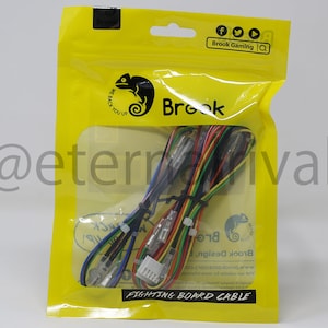 May include: A yellow plastic bag with a clear window showing a multi-colored cable with connectors. The bag has a black chameleon logo with the text "Brook" and "We Back You Up!" printed on it. The text "Fighting Board Cable" is printed on the bottom of the bag.