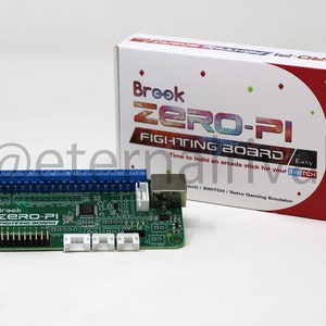 May include: A green circuit board with the text "Brook ZERO-PI FIGHTING BOARD" printed on it. The board has a USB connector, a row of blue connectors, and several white connectors. The board is next to a red box with the text "Brook ZERO-PI FIGHTING BOARD" printed on it. The box also has the text "Time to build an arcade stick for your SWITCH / SWITCH / Retro Gaming Emulator" printed on it.