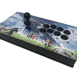 May include: A rectangular arcade controller featuring a black joystick and eight black circular buttons on the right side. The top surface displays a colorful graphic illustration of fantasy characters in a grassy field under a cloudy sky.