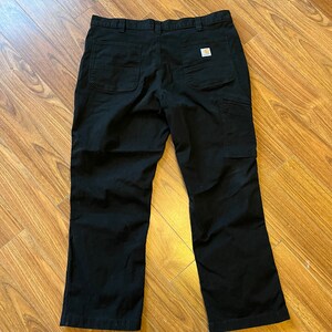 May include: Black work trousers with a Carhartt logo patch on the back right pocket.