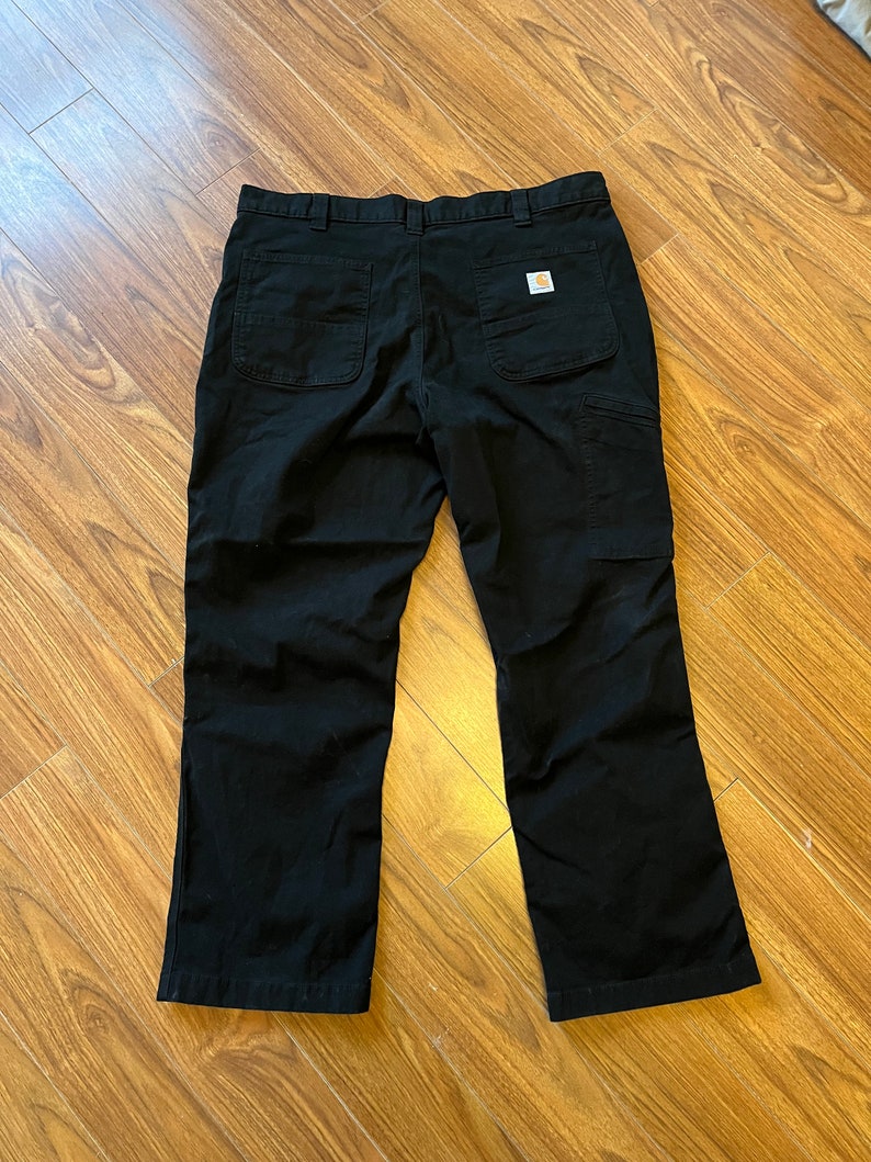 May include: Black work trousers with a Carhartt logo patch on the back right pocket.