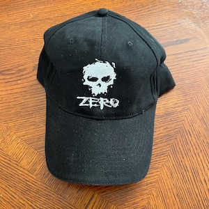 May include: Black baseball cap with a white skull and crossbones graphic and the word "ZERO" embroidered on the front.