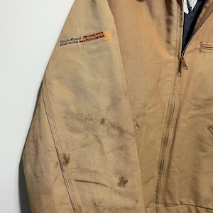 Puede incluir: Chaqueta de trabajo color canela con cuello de pana marr&oacute;n y cremallera completa. La chaqueta tiene un peque&ntilde;o logotipo bordado en la manga izquierda y algunas manchas. La chaqueta est&aacute; hecha de un material duradero y resistente.