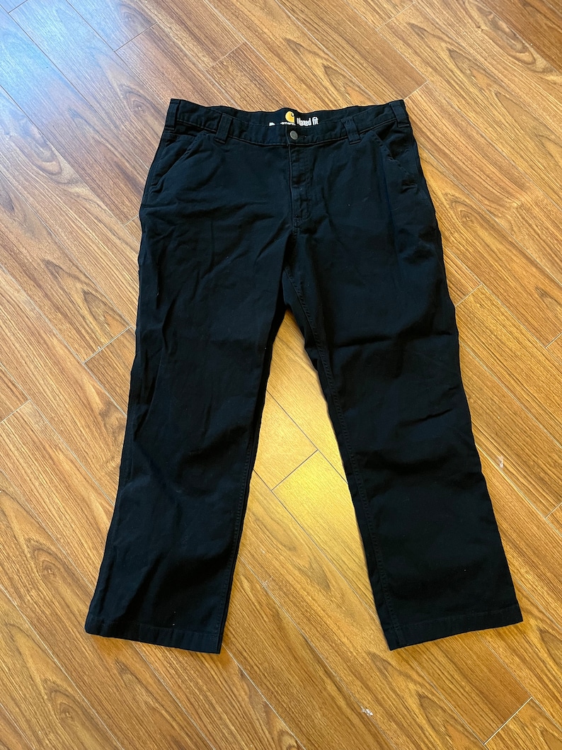 May include: Black work trousers with a straight fit and a Carhartt label on the waistband.