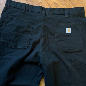 May include: Black work trousers with two back pockets and a Carhartt logo patch on the right back pocket.
