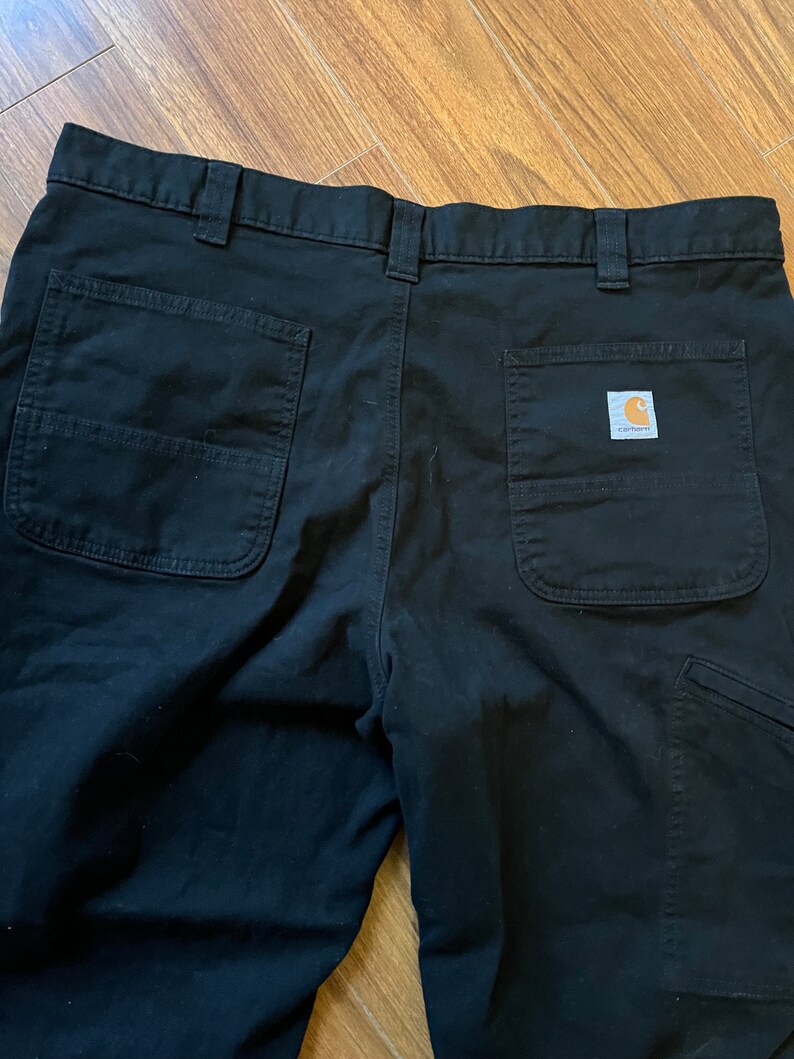 May include: Black work trousers with two back pockets and a Carhartt logo patch on the right back pocket.