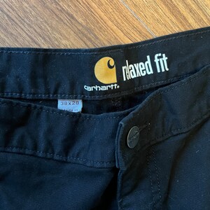 May include: Black Carhartt relaxed fit trousers with a yellow tag that says "relaxed fit" and "Carhartt". The tag also has a size label that says "38 x 28" and "made in".