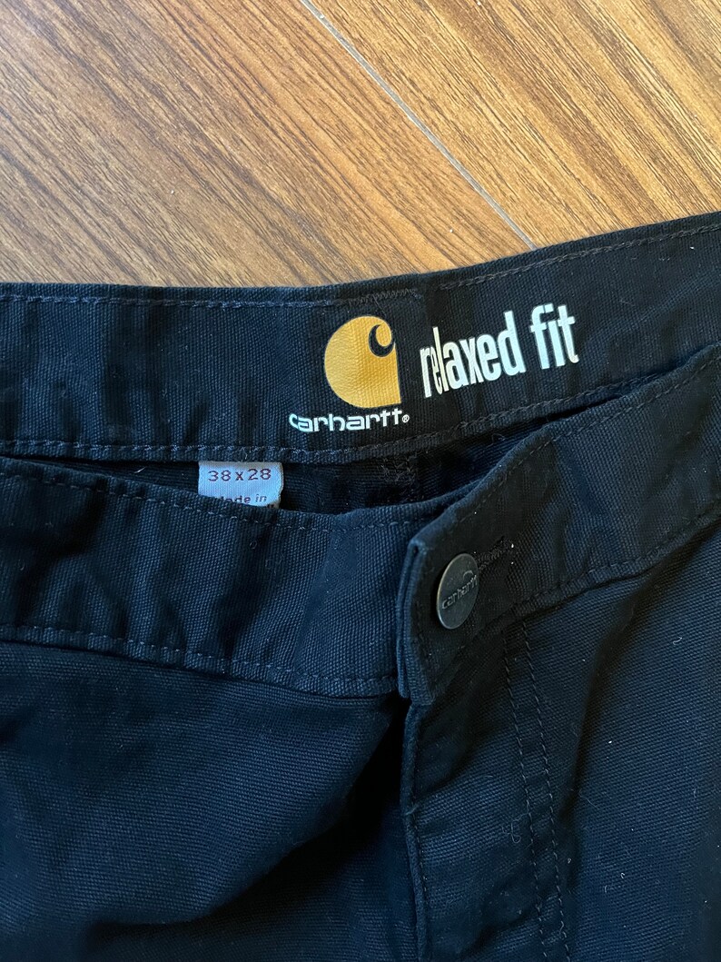 May include: Black Carhartt relaxed fit trousers with a yellow tag that says "relaxed fit" and "Carhartt". The tag also has a size label that says "38 x 28" and "made in".