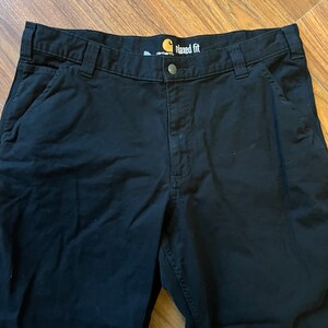 May include: Black Carhartt work trousers with a relaxed fit. The trousers have a label that says "Carhartt" and "Maxed Fit".