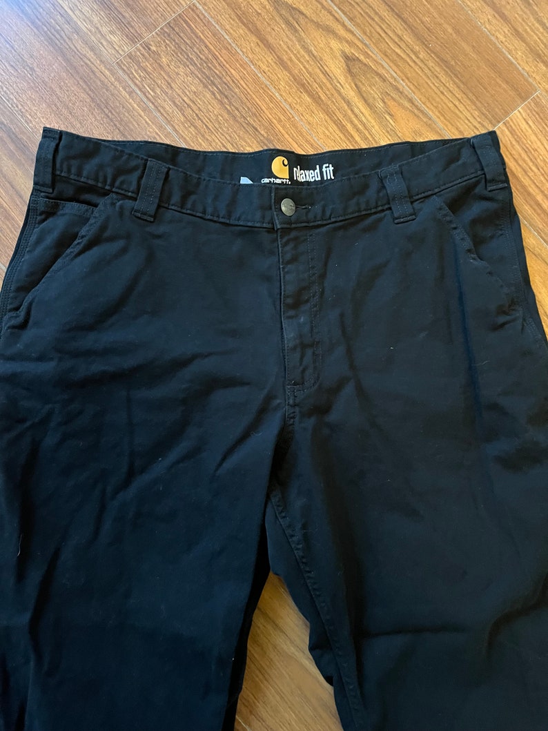 May include: Black Carhartt work trousers with a relaxed fit. The trousers have a label that says "Carhartt" and "Maxed Fit".