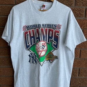 May include: A gray t-shirt with a graphic of the New York Yankees 1996 World Series Champions logo. The logo features a baseball diamond with the team's logo, a baseball, and the words "World Series" and "Champs".