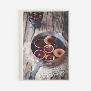 May include: A copper pot filled with red wine, orange slices, and spices sits on a rustic wooden surface. The pot has a long handle and is surrounded by a burlap cloth.