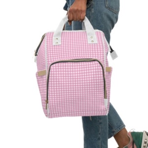 K&ouml;nnte beinhalten: Rosa-wei&szlig;e Gingham-Wickeltasche mit Rei&szlig;verschluss-Vordertasche und verstellbaren Tr&auml;gern.