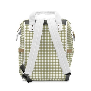 K&ouml;nnte beinhalten: Ein gr&uuml;ner und wei&szlig;er karierter Rucksack mit wei&szlig;en verstellbaren Tr&auml;gern und schwarzen Schnallen.