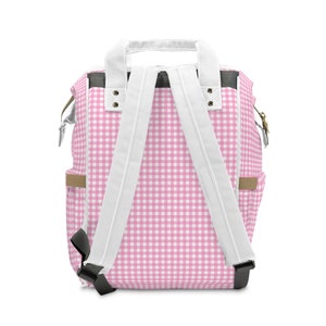 K&ouml;nnte beinhalten: Rucksack mit pink-wei&szlig;em Karomuster, wei&szlig;en Tr&auml;gern und schwarzen Akzenten.
