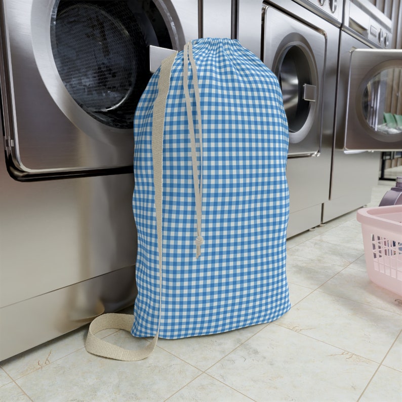 Puede incluir: Una bolsa de lavander&iacute;a de gingham azul y blanco con cierre de cord&oacute;n y una correa larga de color beige.