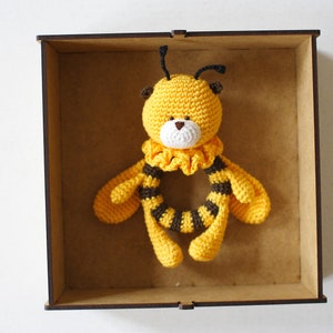 May include: A handmade crochet bee rattle in a wooden box. The bee is yellow with black stripes and a white face. The rattle is designed for babies and young children.