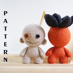 May include: Two crocheted amigurumi toys. One is a beige creature with a button eye and a stitched mouth. The other is an orange creature with a black crocheted flower on top.