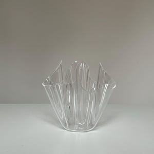 May include: A clear, decorative glass bowl with a unique, ruffled design. The bowl has a wide, open top and a series of vertical ridges that create a textured appearance. The bowl is made of transparent glass and is suitable for decorative purposes.