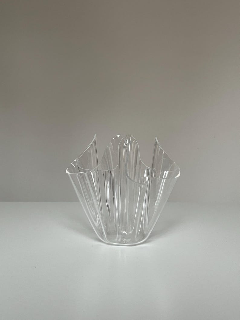 May include: A clear, decorative glass bowl with a unique, ruffled design. The bowl has a wide, open top and a series of vertical ridges that create a textured appearance. The bowl is made of transparent glass and is suitable for decorative purposes.