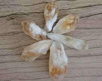 May include: Six raw, pointed, light brown and white citrine crystals arranged in a starburst pattern on a wood surface.
