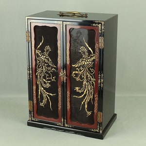 Puede incluir: Un gabinete lacado en negro con dos puertas, que presenta diseños de fénix dorados sobre un fondo rojo. El gabinete tiene una manija de latón y detalles decorativos.