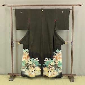 May include: A black kimono with a colorful floral pattern featuring a scene with trees and figures. The kimono is displayed on a wooden rack.