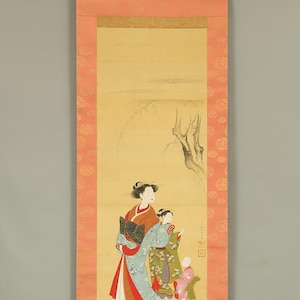 May include: A vertical hanging scroll featuring a painting of three figures in traditional attire. The central figure wears a blue patterned kimono with a red underlayer, while two smaller figures wear green and pink patterned garments.