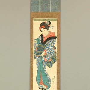 May include: Japanese woodblock print of a woman in a floral kimono. The print is mounted on a scroll with a blue patterned top and bottom. The woman's kimono is blue with white flowers and a red and black collar.