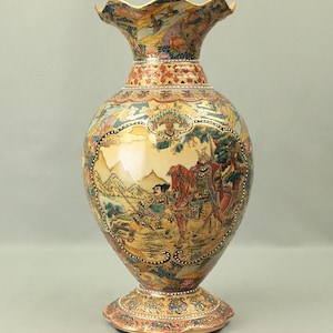 Può includere: Un vaso in ceramica alto e ornato con bordo svasato e base ampia. Il vaso presenta scene dettagliate dipinte a mano di figure a cavallo e in paesaggi, con dettagli dorati e bordo smerlato. La tavolozza dei colori include beige, rosso, blu e oro.