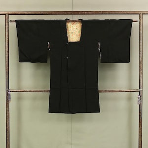 May include: A black kimono with a colourful floral pattern lining the collar. The kimono is hanging on a wooden rack.