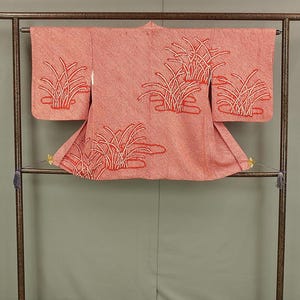 Puede incluir: Un kimono rosa con un diseño de hierba roja y blanca colgado en un estante de madera.