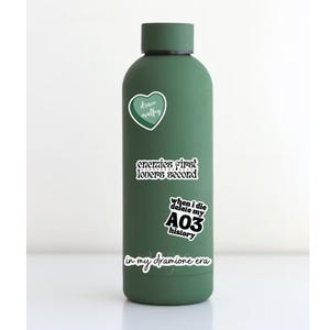 Puede incluir: Una botella de agua reutilizable verde con varias pegatinas. Las pegatinas incluyen un coraz&oacute;n con el texto "draco malfoy", una pegatina con el texto "enemies first lovers second", una pegatina con el texto "when i die delete my A03 history", y una pegatina con el texto "in my dramione era".