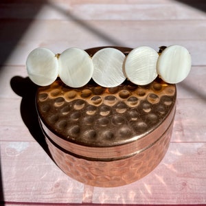 May include: A gold hair clip with five white, round, pearlescent embellishments.